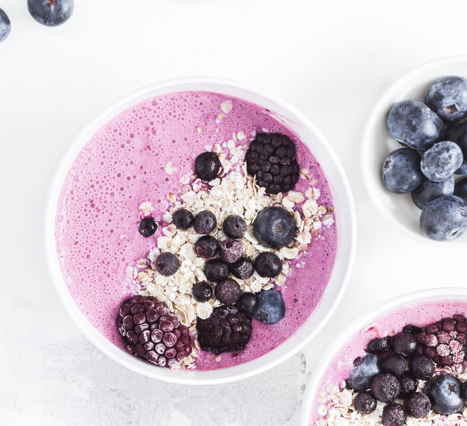 top view shot of a bowl of Annie's Immunity Acai frozen smoothie topped with blueberries, blackberries and oats beside a bowl of blueberries and another bowl of frozen smoothie.