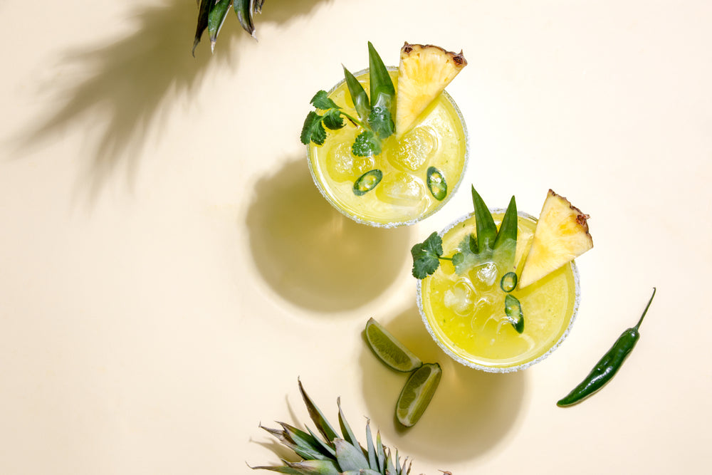 top view of two glasses of iced green jalapeno pineapple chia with sliced of chili and aloe vera and cilantro surrounded by slices of lemon and whole chili