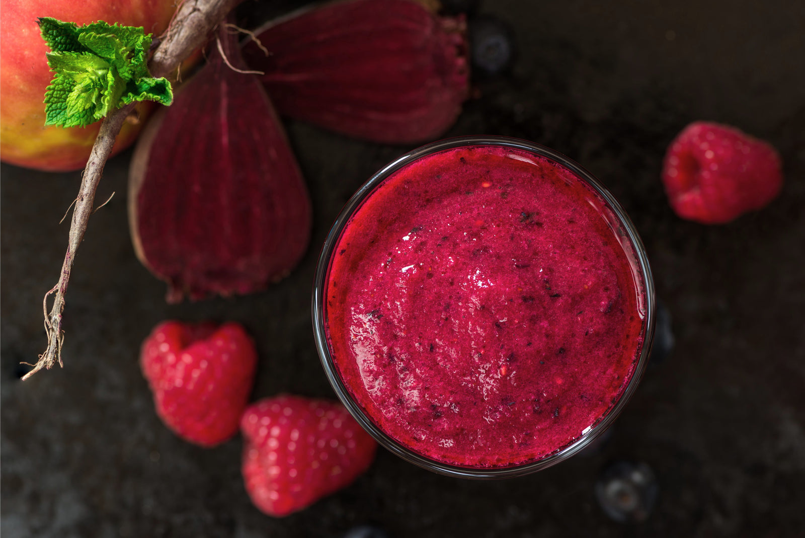 top view shot of a glass of Cherry-Berry Beets Smoothie beside raspberries and sliced beet roots.