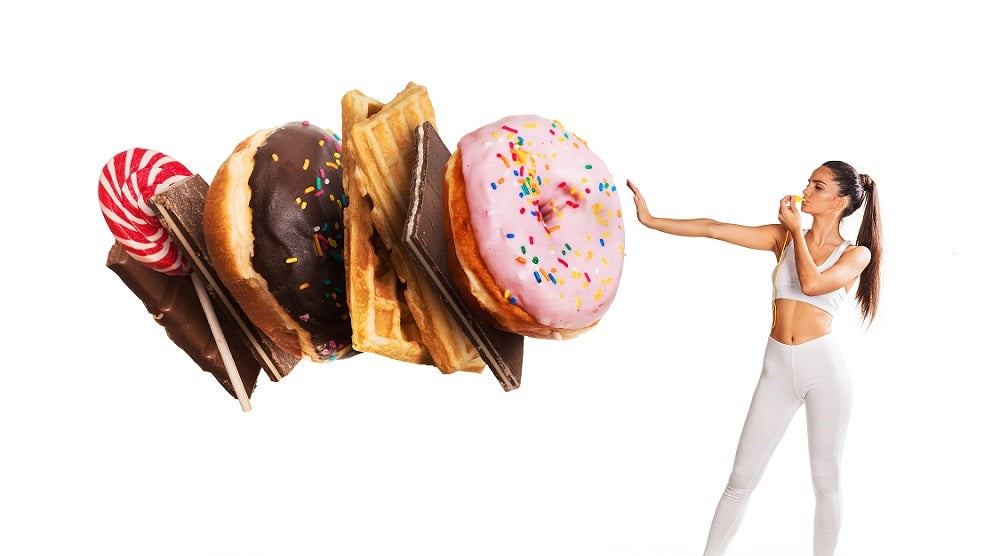 Image of a fit woman wearing a sports wear stopping and blocking some gigantic donuts and pastries. Set against a white background.