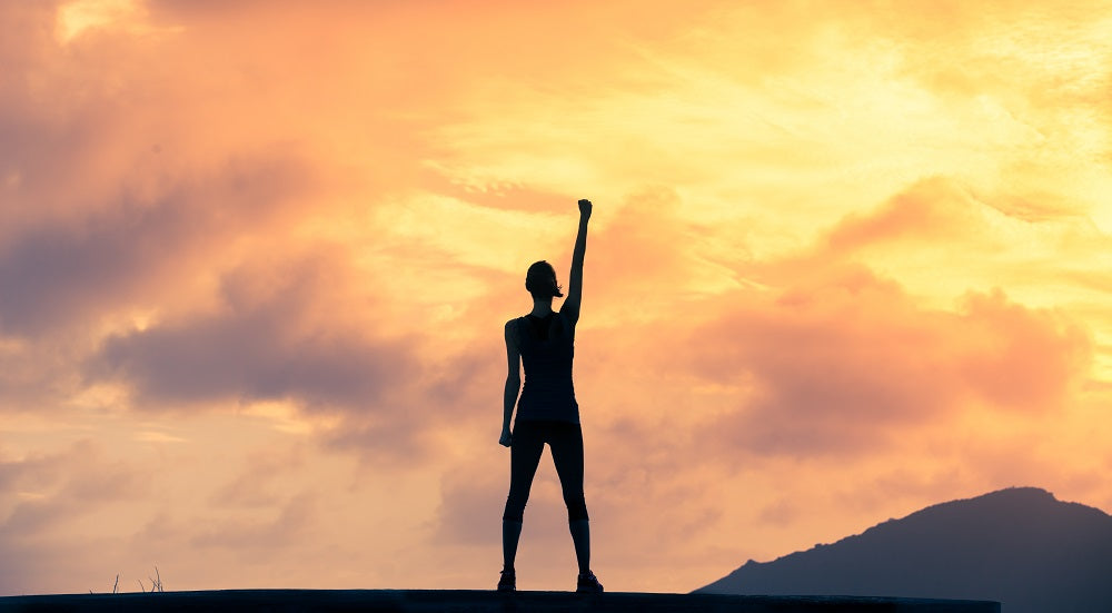 Shadow of a figure standing on top of a mountain with a victory pose at sunset