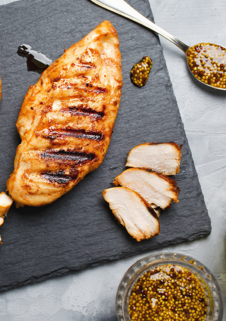 roasted chicken breast beside 2 slices of roasted chicken breast beside a spoon of balsamic vinegar and on the other side is a bowl of balsamic vinegar. 
