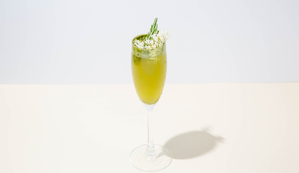 one wine glass of superfood mimosa topped with a white small flower on white background