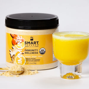1 jar of 150 grams Immunity Wellness, in front is a stirring spoon full of light brown powder and a glass of orange-colored juice against a white background.